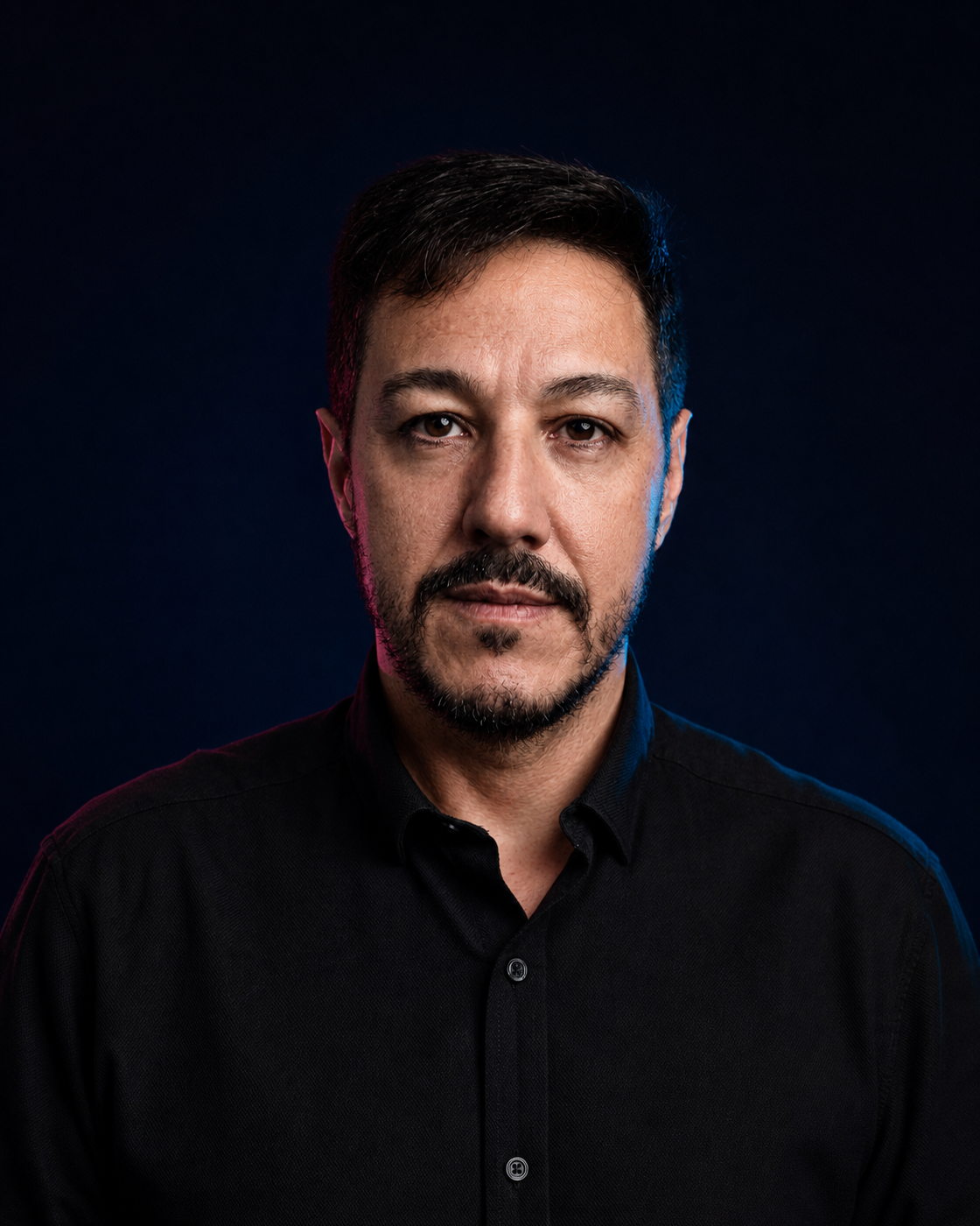 Retrato editorial colorido de Reginaldo Melo, sem óculos, com cabelo curto e barba aparada, sobre fundo navy.